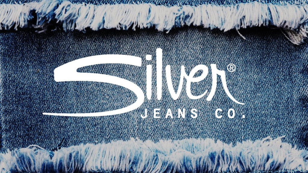 A pitch deck slide with a close-up of frayed denim fabric with the "Silver Jeans Co." logo in white text overlaying the center. The logo features a stylized cursive "Silver" with "JEANS CO." in uppercase letters below it, capturing the essence of premium denim jeans craftsmanship.